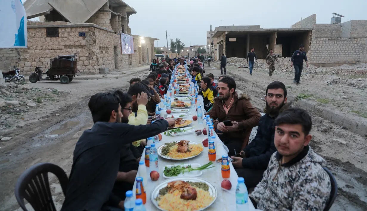 Warga Suriah berkumpul di daerah yang rusak berat untuk berbuka puasa di Tadef, dekat kota perbatasan al-Bab, yang dikendalikan pemberontak yang didukung Turki di Suriah (18/4/2022). Buka puasa ini diselenggarakan oleh sebuah LSM berkoordinasi dengan berbagai faksi lokal. (AFP/Bakr Alkasem)