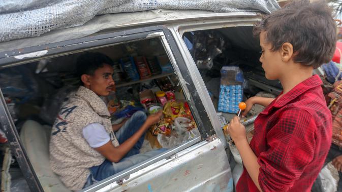 Majd al-Din al-Shamiri (16) melayani pembeli di toko darurat di kawasan Jabal Sabr, Yaman pada 28 September 2019. Majd al-Din al-Shamiri mengubah mobil keluarganya yang rusak parah, akibat perang yang melanda, menjadi toko darurat untuk membantu keluarganya mencari nafkah. (Ahmad AL-BASHA/AFP)
