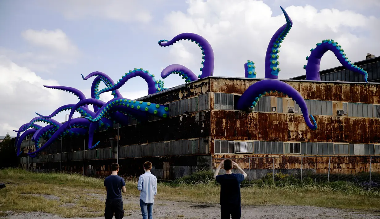 Pengunjung mengambil gambar patung karet "Sea Monsters HERE" di gudang berkarat Building 61 di Navy Yard, Philadelphia, Selasa (9/10). Kreasi sepanjang 40 kaki ini menampilkan tentakel ungu besar yang keluar dari jendela hingga ke atap. (AP/Matt Rourke)