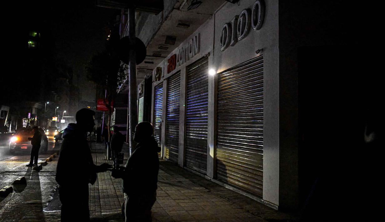 Kebijakan ini direncanakan berlaku selama satu bulan sebelum dievaluasi kembali. Tampak dalam foto, orang-orang berdiri di dekat toko-toko yang tutup lebih awal karena jam malam yang diberlakukan pemerintah untuk mengurangi biaya energi di pusat kota Kairo, Mesir, pada Kamis 2 April 2026. (Khaled DESOUKI/AFP)