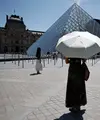 Seseorang berlindung di bawah payung di depan museum Louvre di Paris saat gelombang panas yang memecahkan rekor melanda sebagian besar Eropa Barat pada Kamis 28 Mei 2026. (SIMON WOHLFAHRT/AFP)