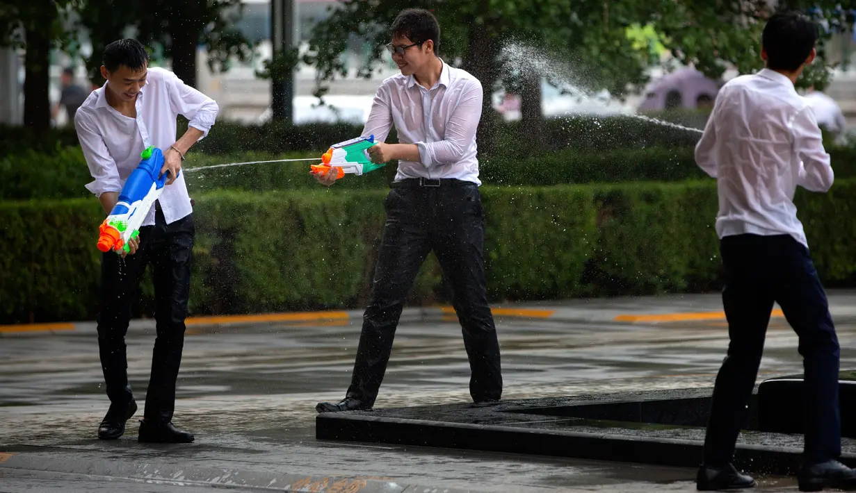 Tiga pekerja kantor bermain senjata air di luar gedung kantor, Beijing, (13/7). Karyawan di China terkadang menghabiskan waktu berjam-jam di tempat kerja dan beralih bermain dengan ide kreatif untuk menghilangkan stres. (AP Photo/Mark Schiefelbein)