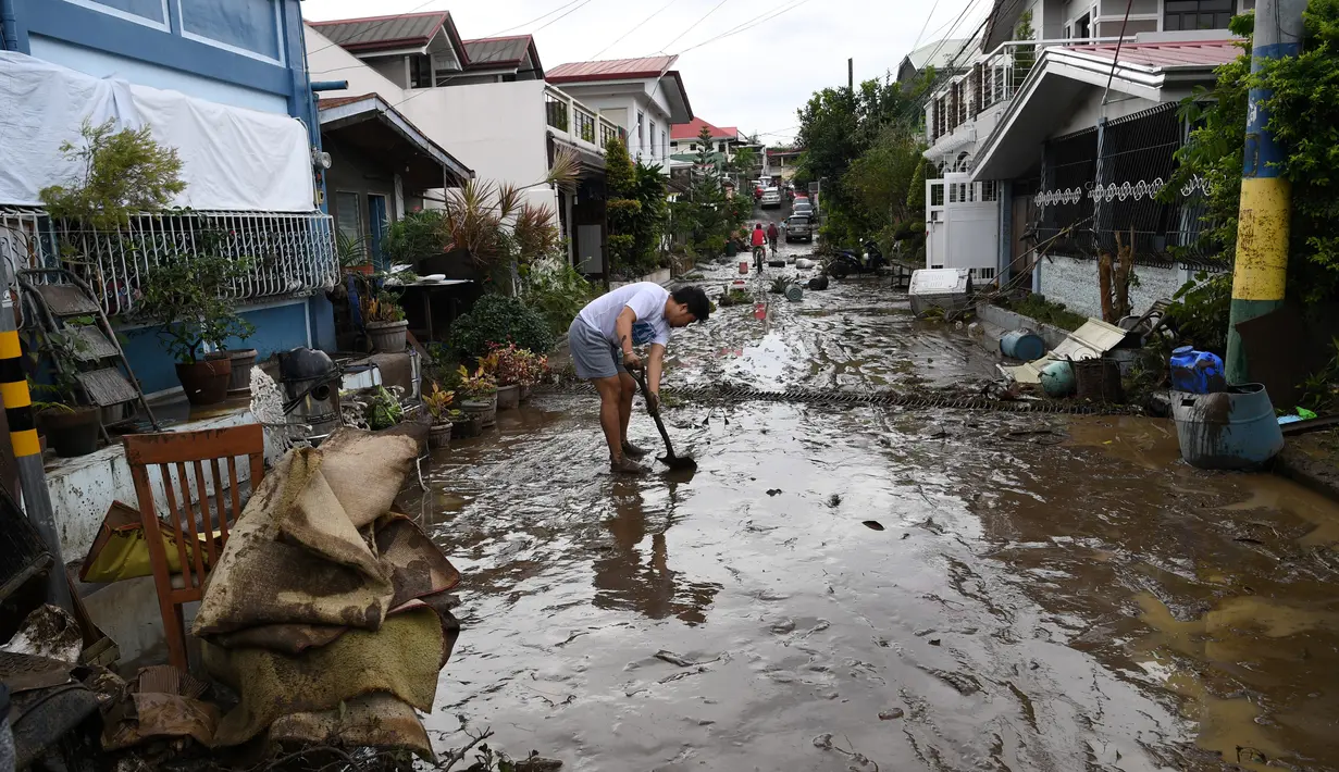 Seorang warga menyekop lumpur dari jalananan setelah banjir akibat Topan Goni di Kota Batangas, selatan Manila, Filipina, Senin (2/11/2020). Badan Bencana Negara mencatat sedikitnya 16 orang tewas akibat topan terkuat di dunia tahun ini, yang menghantam Filipina pada hari Minggu. (TED ALJIBE / AFP)