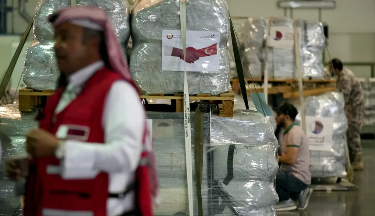 Karyawan Bulan Sabit Merah Qatar memegang spanduk berisi paket bantuan yang akan dikirim untuk wilayah yang terkena gempa di Turki, di Pangkalan Udara Al-Udeid di Qatar, Selasa, 7 Februari 2023. Gempa bumi dahsyat melanda Turki tenggara dan Suriah Senin dini hari, merobohkan ratusan bangunan serta menewaskan dan melukai ribuan orang. (AP Photo/Kamran Jebreili)