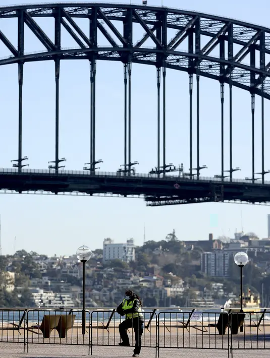 Seorang pejabat keamanan berdiri di depan Harbour Bridge, Sydney, Australia, Selasa (13/7/2021). Lima juta penduduk Sydney akan berada dalam lockdown COVID-19 untuk dua minggu lagi. (Brendon THORNE/AFP)