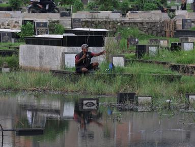 Seorang warga memancing ikan di Taman Pemakaman Umum (TPU) Tanah Kusir, Jakarta Selatan, Jumat (26/8). Warga memanfaatkan Banjir yang merendam makam di kawasan tanah kusir ini terjadi akibat luapan Sungai Pesanggrahan. (Liputan6.com/Johan Tallo)