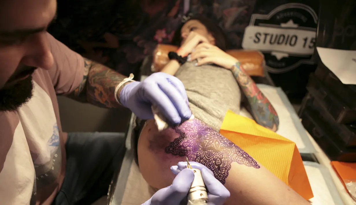 Seorang seniman membuat tato di paha pelanggannya saat acara Festival Tato Internasional di Sochi, Rusia, (23/4). Sejumlah wanita tampak antusias untuk mentato tubuhnya di festival tato terbesar di negara tersebut. (REUTERS/Kazbek Basayev)