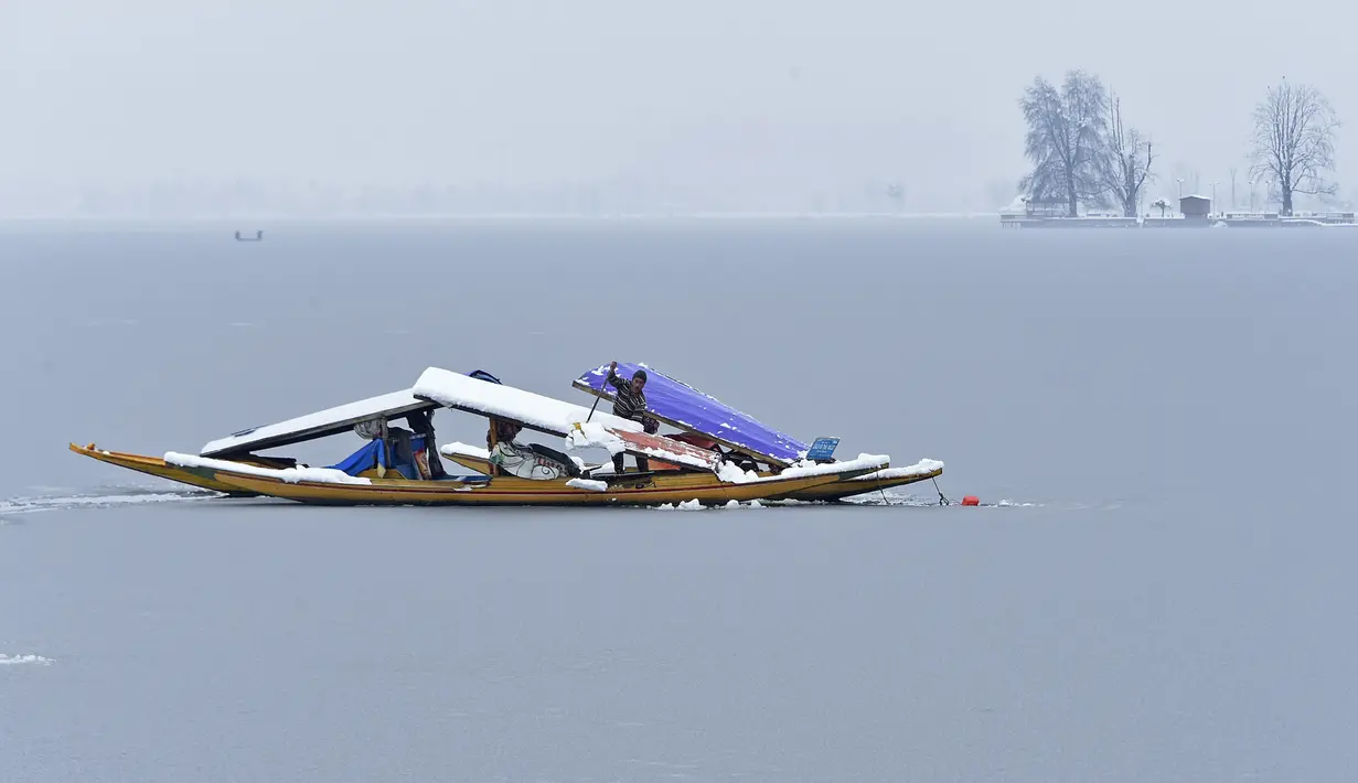 Seorang lelaki menyingkirkan salju dari sebuah kapal dekat bagian beku danau Dal setelah hujan salju lebat di Srinagar (16/1/2020). Sebagian danau yang terkenal itu, juga objek wisata, telah membeku ketika wilayah itu mencatat malam terdingin pada 28 Desember. (AFP Photo/Tauseef Mustafa)