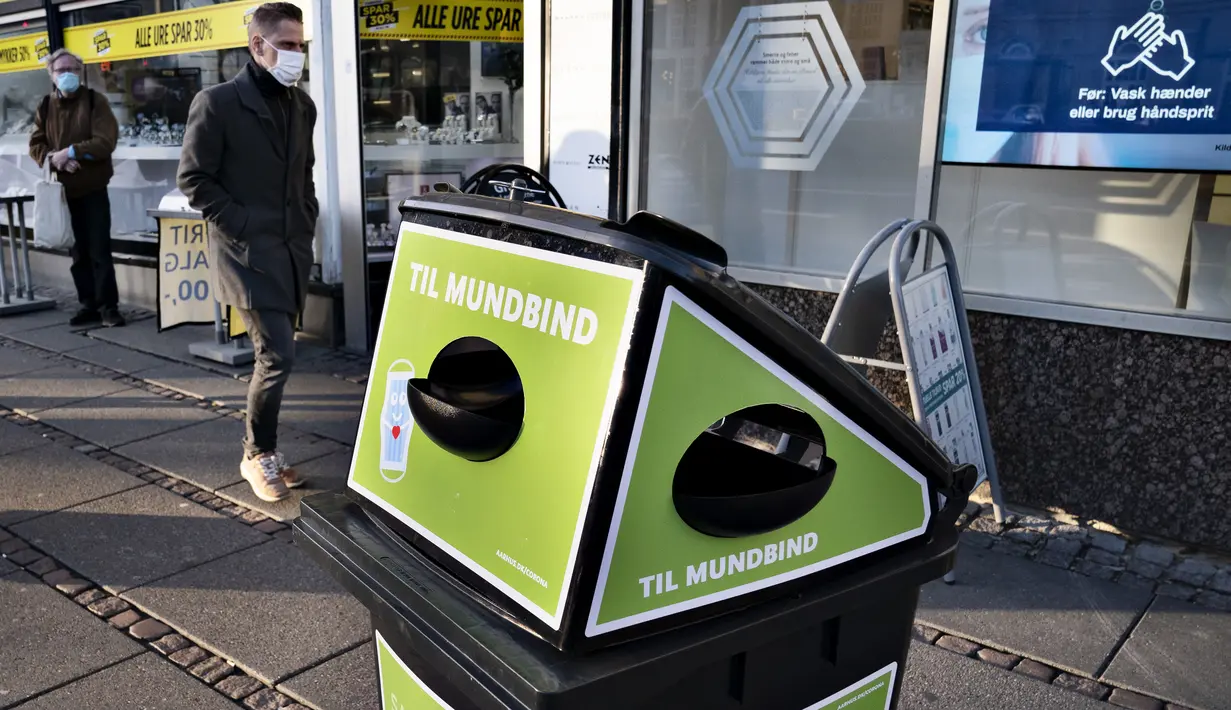 Pejalan kaki berjalan melewati tempat sampah untuk masker sekali pakai, di Aarhus Center, Denmark, Senin (23/11/2020). Kota Aarhus menempatkan seratus tempat sampah khusu berukuran 240 liter yang dapat menampung sekitar 3000 masker bekas. (Henning Bagger/Ritzau Scanpix/AFP)