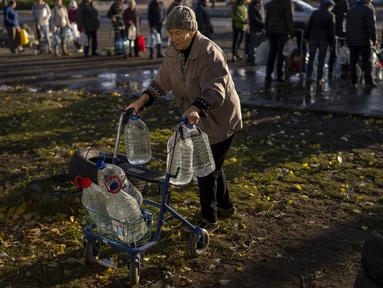 Perempuan lansia mendorong alat bantu jalan yang penuh dengan botol plastik setelah diisi ulang ke dalam tangki, di pusat kota Mykolaiv, Ukraina, Senin (24/10/2022). Sejak pertengahan April warga Mykolaiv telah hidup tanpa pasokan air minum. (AP Photo/Emilio Morenatti)