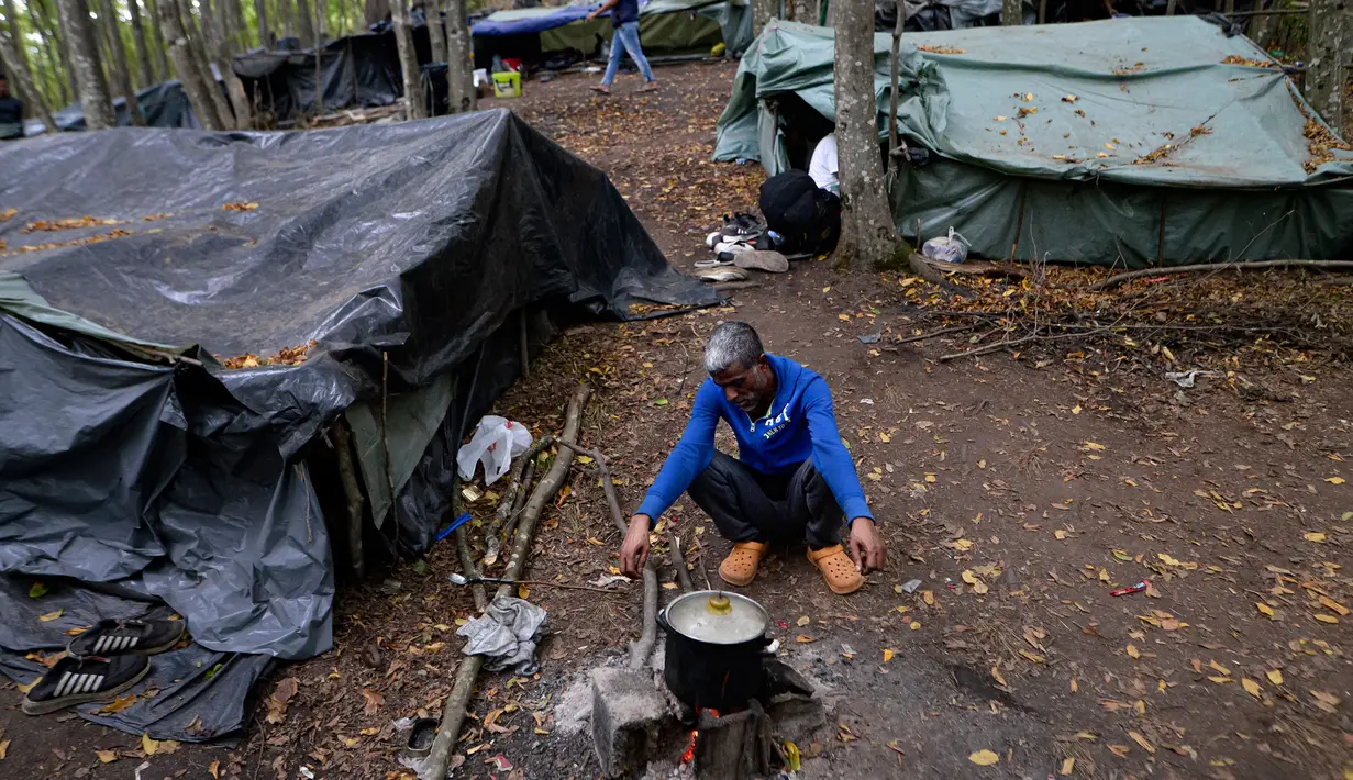 Seorang migran memasak dengan api terbuka di kamp darurat di hutan di luar Velika Kladusa, Bosnia pada 25 September 2020. Kebanyakan imigran dan pengungsi di Bosnia berasal dari Timur Tengah, Afrika dan Asia. (AP Photo/Kemal Softic)
