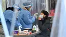 Petugas medis (tengah) mengambil sampel usap hidung dari seorang wanita di pusat pengujian virus corona COVID-19, Seoul, Korea Selatan, Rabu (16/2/2022). Kasus COVID-19 harian Korea Selatan meningkat tajam mencapai angka tertinggi baru yaitu lebih dari 90 ribu. (Jung Yeon-je/AFP)