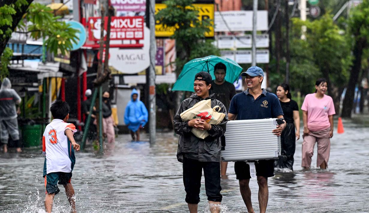 Banjir yang melanda Denpasar terjadi akibat meluapnya saluran drainase yang tidak mampu menampung debit air hujan. Tampak dalam foto, para tamu hotel membawa koper mereka sambil menerobos air di jalan yang tergenang banjir akibat hujan lebat di Legian Kuta, Denpasar, Bali, pada Selasa 24 Februari 2026. (SONNY TUMBELAKA/AFP)