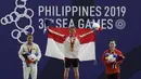 Lifter Aisyah Windy mengibarkan bendera saat naik podium usai mendapatkan medali emas SEA Games 2019 cabang angkat besi nomor 49 kg di Stadion Rizal Memorial, Manila, Minggu (1/12). Dirinya meraih emas dengan total angkatan 104 kg. (Bola.com/M Iqbal Ichsa