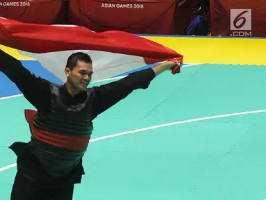 Pesilat Indonesia, Aji Bangkit Pamungkas mengibarkan bendera Merah Putih usai mengalahkan pesilat Singapura Sheik Alauddin dalam babak final Kelas I Putra Asian Games 2018 di TMII, Jakarta, Senin (27/8). (Merdeka.com/Arie Basuki)