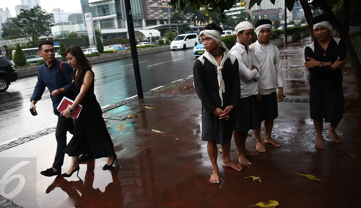 Empat warga Baduy berteduh ketika hujan mengguyur kawasan Bundaran HI, Jakarta, Selasa (6/9). Warga Baduy berjalan ratusan kilometer dari kampung mereka tanpa alas kaki dan sama sekali tidak menggunakan kendaraan bermotor. (Liputan6.com/Faizal Fanani)