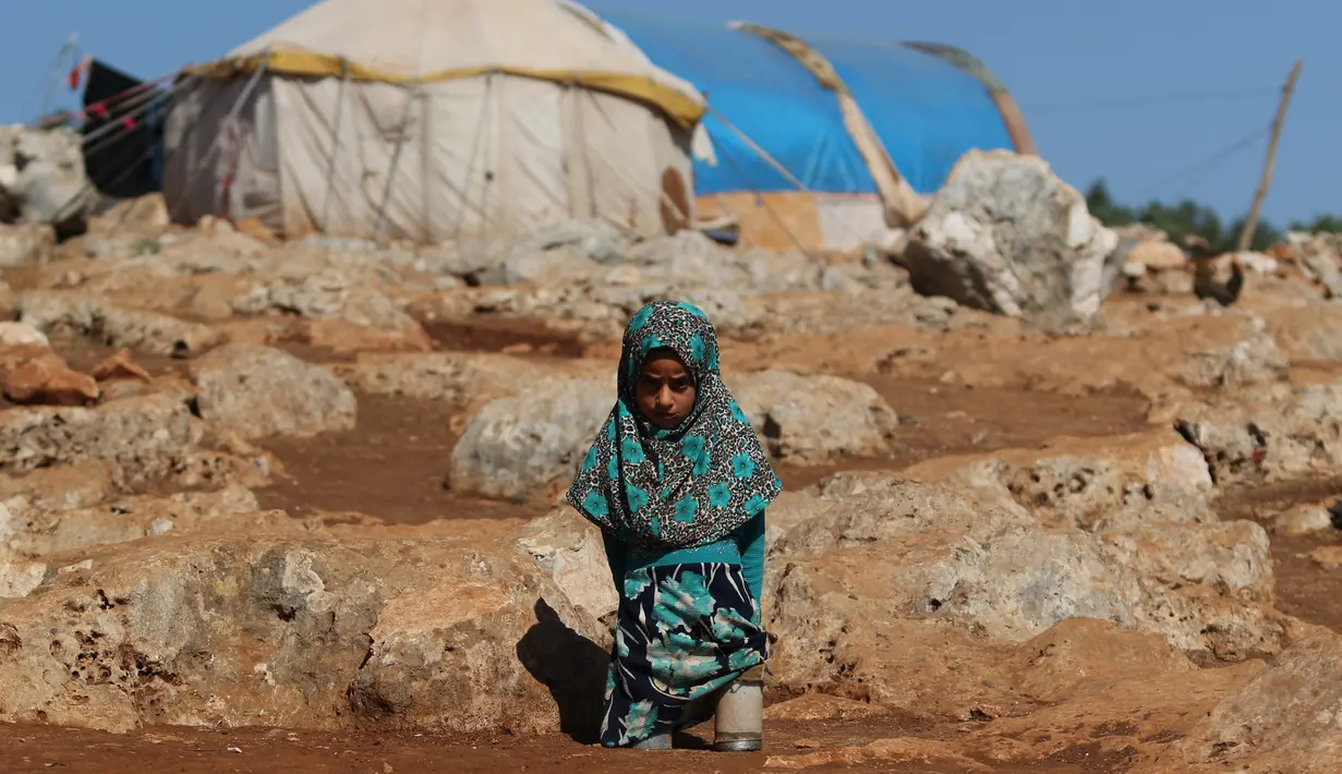Maya Mohammad Ali Merhi (8) berpose menggunakan kaki prostetik dari kaleng di sebuah kamp orang terlantar di Provinsi Idlib, Suriah, Rabu (20/6). (Aaref Watad/AFP)