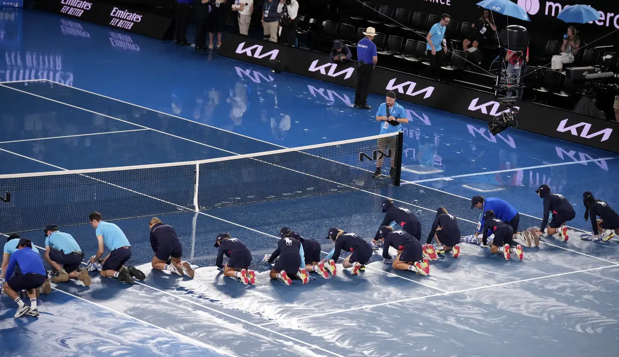 Para ball boy mengeringkan lapangan saat hujan menunda pertandingan perempat final kejuaraan tenis Australia Open 2023 di Melbourne, Selasa (24/1/2023). Setelah hujan berhenti, ball boy dan staf lapangan yang bertugas segera terjun ke lapangan bersama-sama mengeringkan lapangan. (AP Photo/Dita Alangkara)