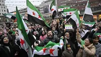 Kekuasaan keluarga Assad di Suriah runtuh dengan sangat cepat setelah kelompok pemberontak keluar dari wilayah yang dikuasainya. Tampak dalam foto, anggota komunitas Suriah memegang bendera oposisi Suriah saat mereka berkumpul pada tanggal 8 Desember 2024 di Sergel's Square di Stockholm, Swedia. (Jonas EKSTROMER/TT News Agency/AFP)