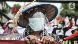 Buruh tani mengenakan faceshield saat ikut dalam aksi menolak UU Omnibus Law Cipta Kerja di Jalan Salemba Raya, Jakarta, Selasa (20/10/2020). Mereka juga mendesak Presiden Joko Widodo segera menerbitkan Perppu pembatalan UU Cilaka. (merdeka.com/Iqbal S. Nugroho)