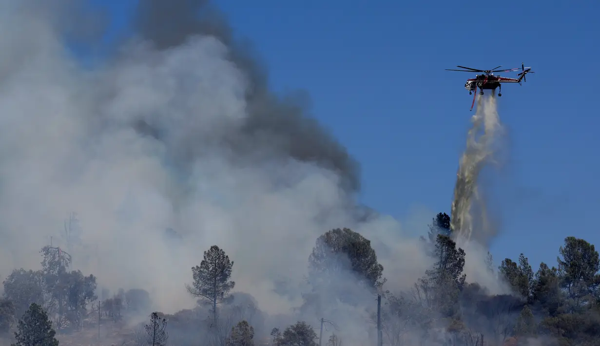 Sebuah helikopter pemadam kebakaran menjatuhkan air di Oak Fire di dekat Mariposa, California (23/7/2022). Api yang bergerak cepat membakar di luar Taman Nasional Yosemite telah memaksa evakuasi, menghanguskan lebih dari 11.500 hektar dan telah menghancurkan beberapa rumah sejak mulai Jumat sore. (Justin Sullivan/Getty Images/AFP)