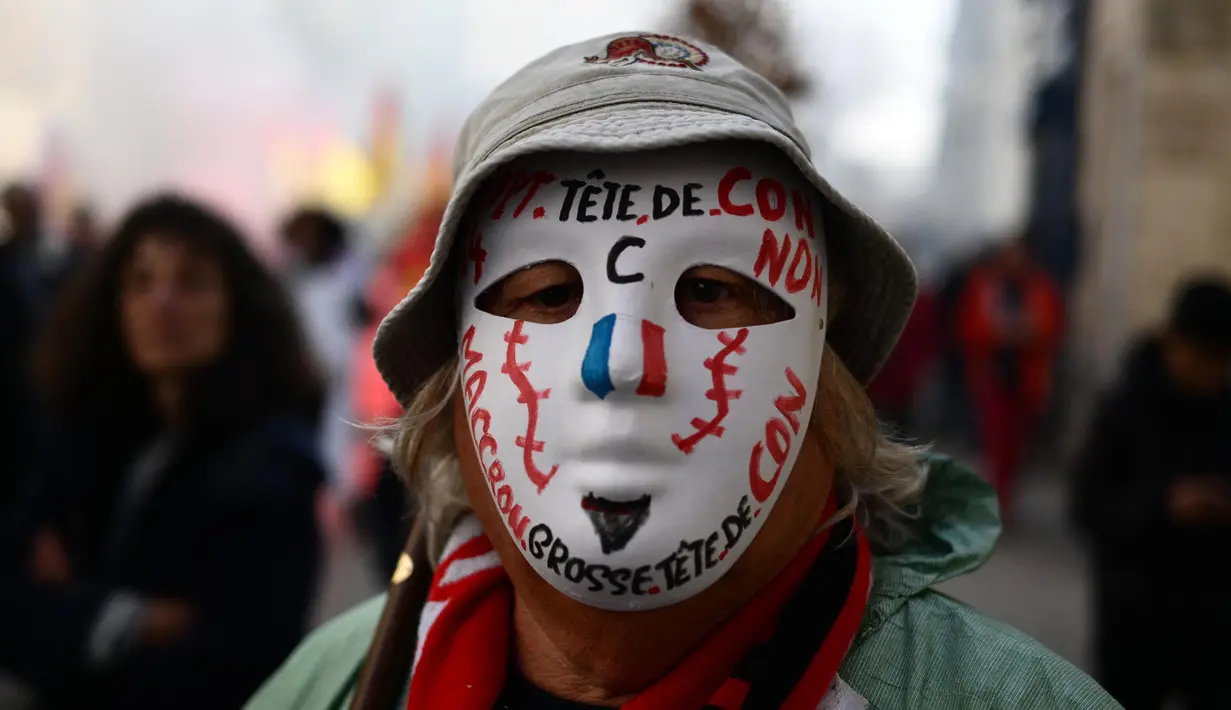 Seorang pengunjuk rasa mengenakan topeng bertuliskan slogan-slogan selama demonstrasi pada hari kelima demonstrasi nasional yang diselenggarakan sejak awal tahun, menentang perombakan pensiun yang sangat tidak populer, di Avignon, Prancis Selatan, Kamis (16/2/2023). (CHRISTOPHE SIMON/AFP)