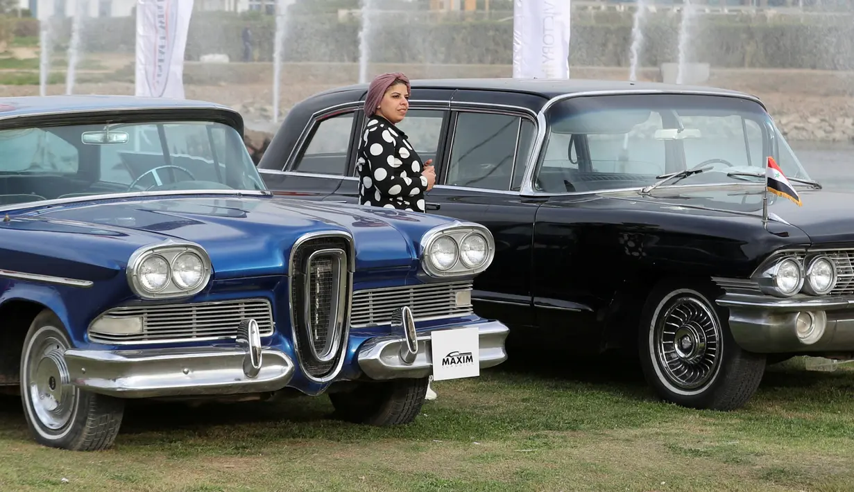 Seorang wanita berdiri di antara Cadillac DeVille hitam dan model DeSoto Fireflite biru selama Pertemuan Klasik Kairo ke-7 di Kairo, Mesir (23/3). (Reuters/Mohamed Abd El Ghany)