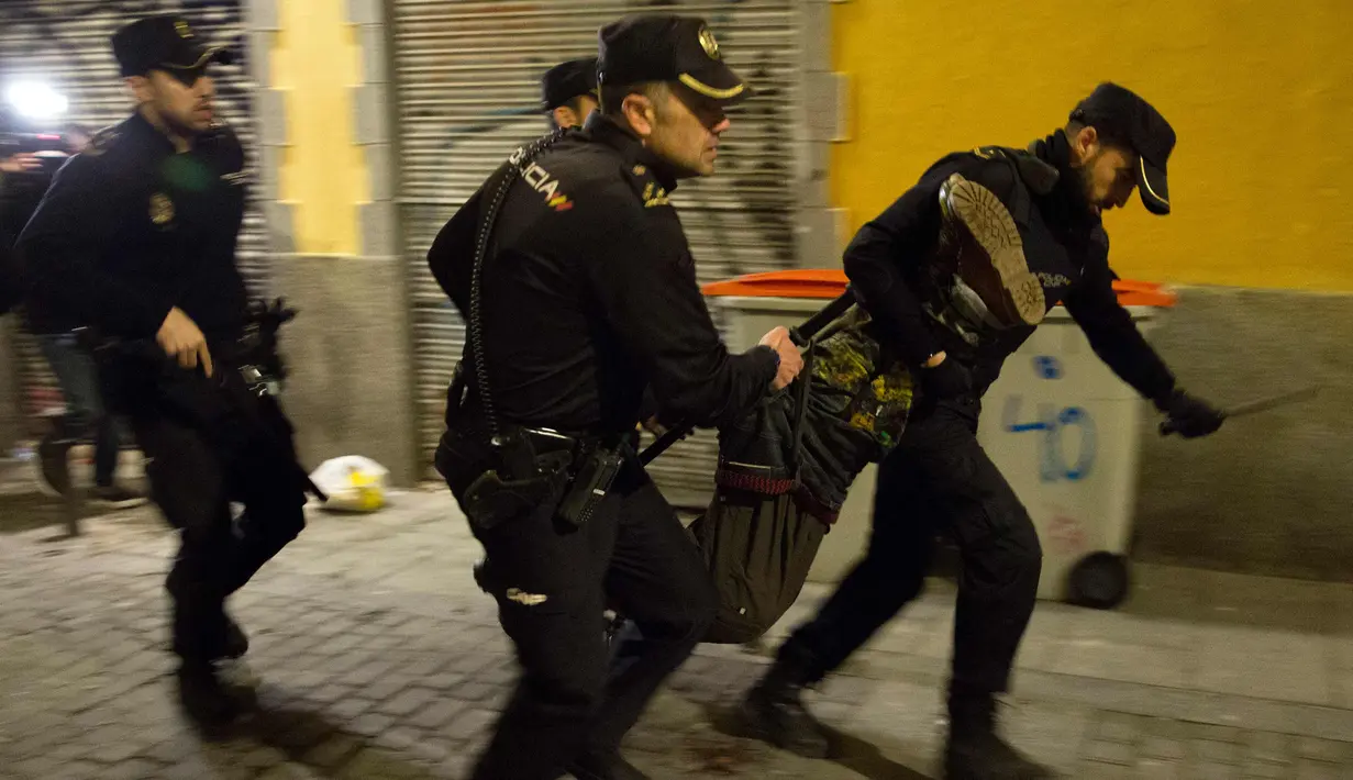 Polisi Spanyol membawa seorang pria saat bentrokan terjadi di Madrid, Spanyol, Kamis (15/3). Bentrokan berawal dari aksi protes imigran atas meninggalnya seorang pedagang jalanan asal Senegal. (AFP Photo/Olmo Calvo)