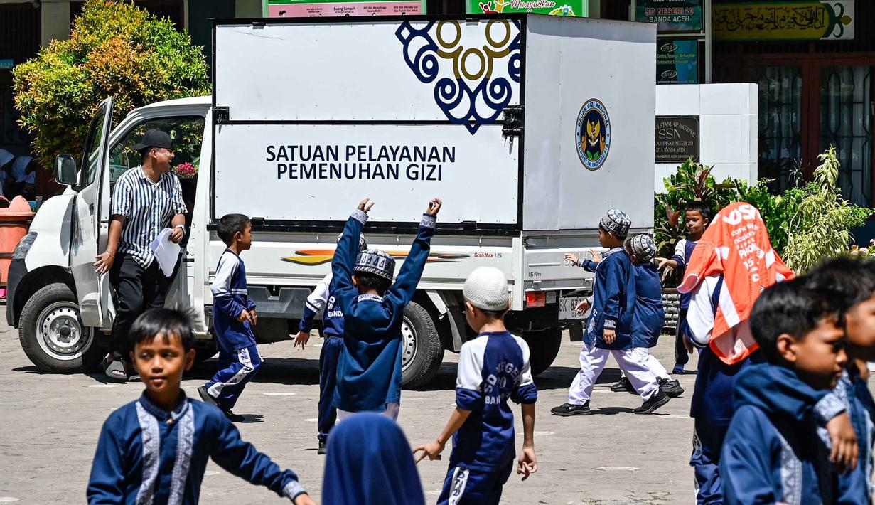 Truk makanan dari program Makan Bergizi Gratis (MBG) terlihat melewati para siswa di sebuah sekolah dasar di Banda Aceh pada Kamis 30 Oktober 2025. Makanan yang sudah disiapkan di dapur SPPG diantar langsung ke sekolah-sekolah dan lokasi penerima. (CHAIDEER MAHYUDDIN/AFP)