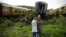 Dua remaja India berswafoto di dekat gerbon kereta yang tergelincir di Asangaon, India (29/8). Sebuah kereta penumpang mengalami kecelakaan di  sekitar 70 kilometer dari Mumbai. (AP Photo / Rafiq Maqbool)