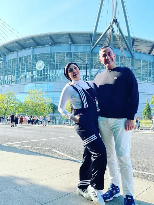 Potret kemesraan Ferdy Hasan dan istri, Safina Hasan di depan markas klub sepak bola Manchester City F.C. Hingga kini, pasangan yang sudah 29 tahun menikah itu jauh dari kabar miring. Keduanya kerap membagikan kemesraan hingga keharmonisan rumah tangganya. [Instagram/ferdyhasan]