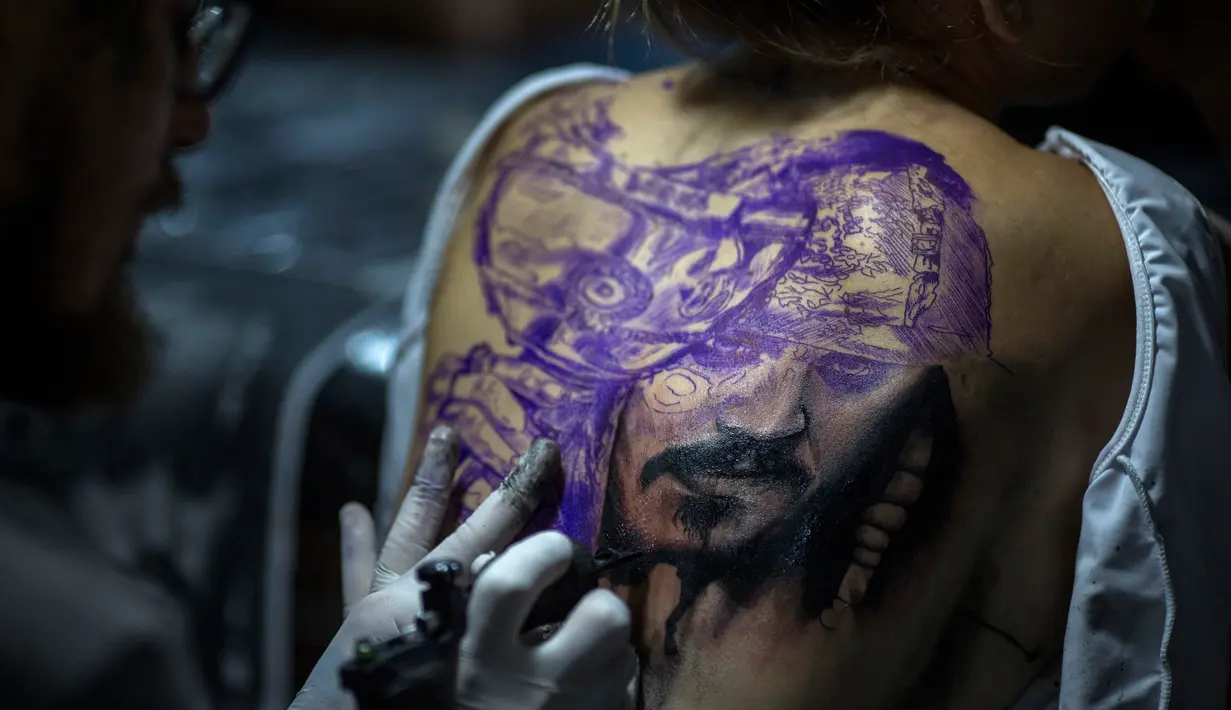 Seorang seniman membuat tato karakter film Pirates of the Caribbean, Jack Sparrow di punggung seorang wanita saat Tattoo Week tahunan di Rio de Janeiro, Brasil (12/1). (AFP Photo/Mauro Pimentel)