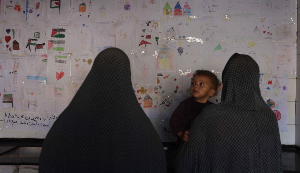 Koleksi gambar-gambar ini berfungsi sebagai medium menyampaikan pesan dan pengalaman hidup anak-anak di zona konflik kepada dunia. Tampak dalam foto, orang-orang melihat pameran yang menampilkan koleksi gambar oleh anak-anak dan perempuan di sebuah sekolah yang diubah menjadi tempat penampungan bagi pengungsi Palestina di kawasan Al-Rimal, Kota Gaza, pada 5 November 2025. (Omar AL-QATTAA/AFP)