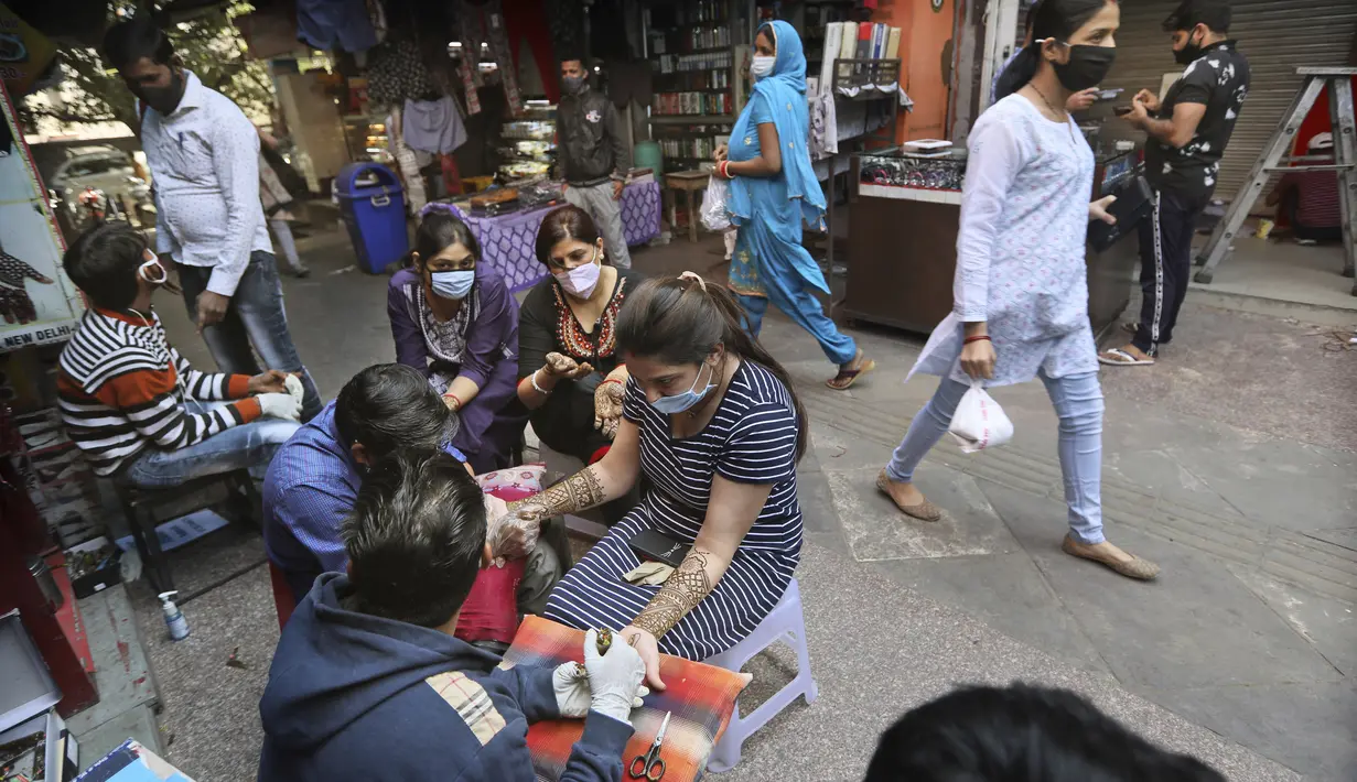 Perempuan yang mengenakan masker mendapatkan desain henna di tangan mereka pada malam festival Karva Chauth di New Delhi, India, Selasa (3/11/2020). Ini adalah festival untuk memulai bulan baru di bulan November di mana para istri akan berpuasa untuk suami-suami mereka. (AP Photo/Manish Swarup)