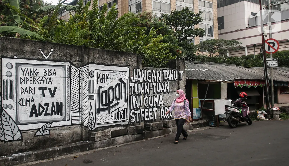 Pejalan kaki melintas di depan mural di kawasan Jakarta Pusat. Selasa (24/8/2021). Mural 'Tuhan Aku Lapar' yang viral di jagat maya pada akhir Juli 2021 lalu, membuka rentetan peristiwa penghapusan mural di kota-kota besar Indonesia. (Liputan6.com/Johan Tallo)