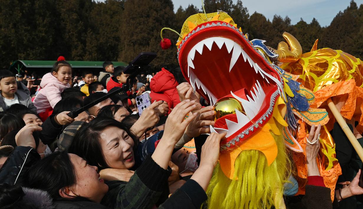 Orang-orang mencoba menyentuh seekor naga saat pertunjukan di sebuah kuil pada hari kedua Tahun Baru Imlek Naga di Beijing pada 11 Februari 2024. (GREG BAKER/AFP)