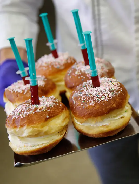 Pekerja berpose sambil membawa berliner (donat Jerman) dengan jarum suntik penuh raspberry jelly di toko roti Kreyenbuhl di Muri, Swiss pada 5 Februari 2021. Merespons hadirnya vaksin Covid-19, toko roti Kreyenbuhl mencoba merayakannya dengan membuat "Vaccine Berliners". (STEFAN WERMUTH/AFP)