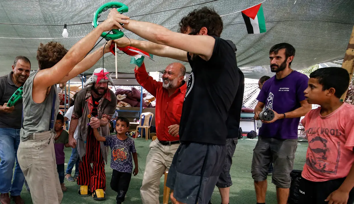 Anak-anak Palestina bermain dengan rombongan badut Spanyol yang tampil menghibur di desa suku Bedouin, Tepi Barat, 22 September 2018. Atraksi ini dilakukan lantaran desa di dekat permukiman Israel itu akan digusur Israel pada Oktober. (AFP/ABBAS MOMANI)
