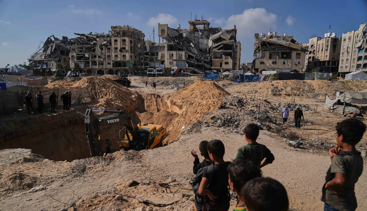 Warga Palestina menyaksikan aktivitas pekerja Mesir yang menggunakan alat berat untuk mencari jenazah para sandera di Kota Hamad, Khan Younis, di Jalur Gaza selatan, Selasa 28 Oktober 2025. (AP Photo/Abdel Kareem Hana)