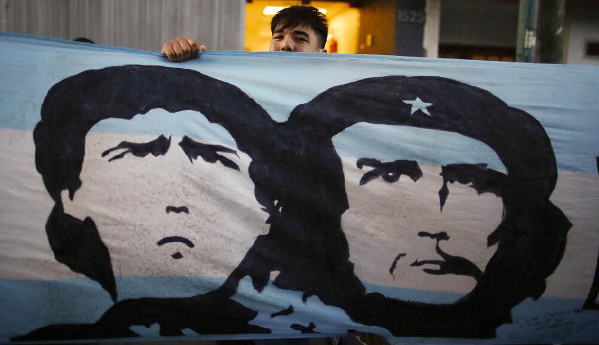 Seorang fans membentangkan bendera bergambar Diego Maradona dan Ernesto "Che" Guevara di depan Rumah Sakit di La Plata, Argentina, Selasa (3/11/2020). Sejumlah fans Argentina berkumpul di depan rumah sakit untuk memberi dukungan kepada sang legenda. (AP/Natacha Pisarenko)