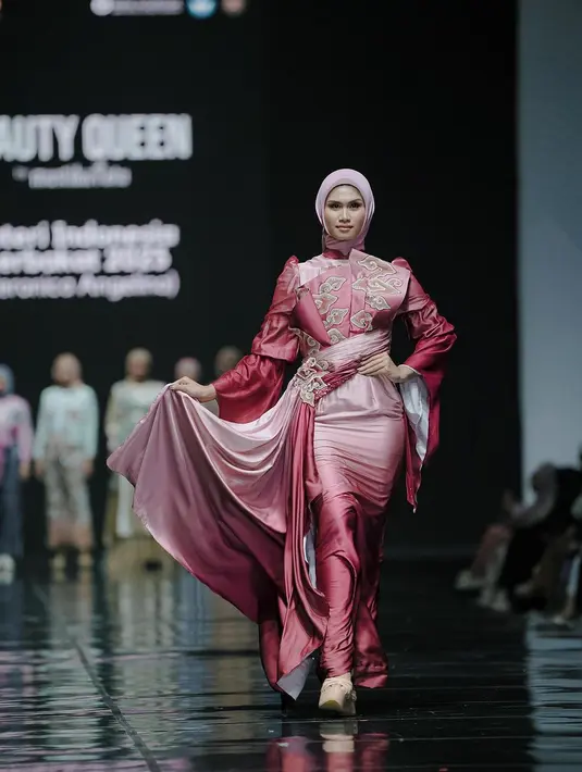 Veronica Angelina tampil glamor dengan gaun gradasi bermotif batik mega mendung. Gaun lengan panjang itu dipadukan dengan belt yang menjuntai dan hijab [@officialputeriindonesia]