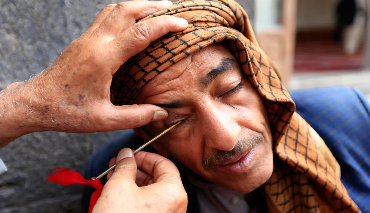 Seorang pria Yaman saat kelopak matanya dirias dengan kosmetik tradisional kohl di Masjid Agung, kota tua Sanaa pada 9 mei 2019. Bagi muslim Yaman, pemakaian kohl diyakini mampu membersihkan dan melindungi mata dari penyakit ini sudah menjadi tradisi setiap bulan Ramadan. (MOHAMMED HUWAIS/AFP)