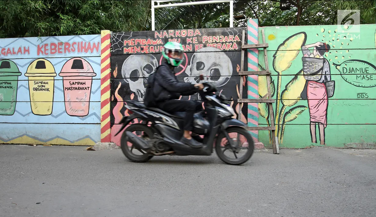Pengendara sepeda motor melintas di sisi tembok yang terdapat lukisan mural di kawasan Kramat Jati, Jakarta, Rabu (4/4). Mural-mural tersebut mengandung pesan kebersihan, bahaya narkoba hingga pencegahan kekerasan. (Liputan6.com/Herman Zakharia)