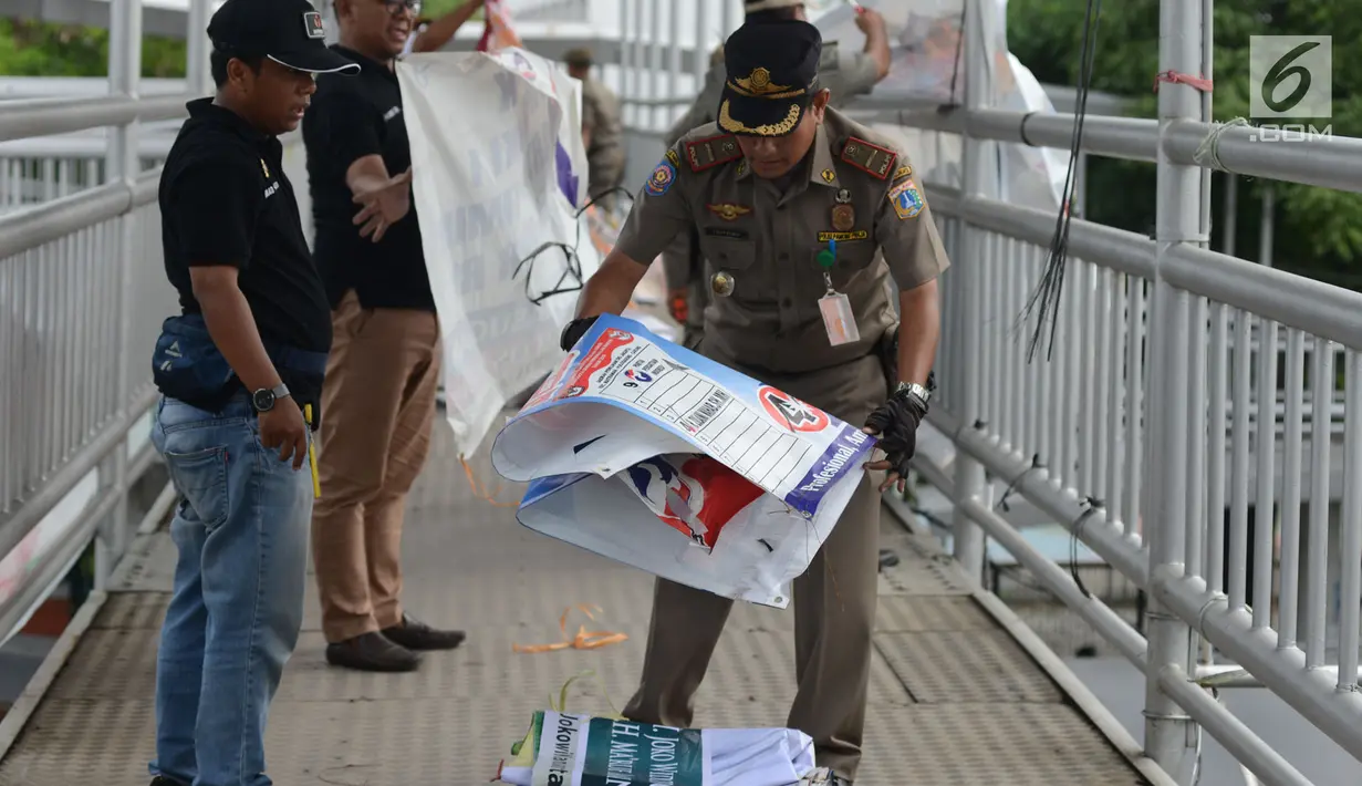 Petugas Satpol PP dan Panwas Pemilu menertibkan Alat Peraga Kampanye (APK) Pilpres, Caleg dan Partai Politik di Kawasan Jalan Pemuda, Jakarta, Rabu (13/3). APK Pemilu 2019 yang terpasang pada JPO dibersihkan. (merdeka.com/Imam Buhori)