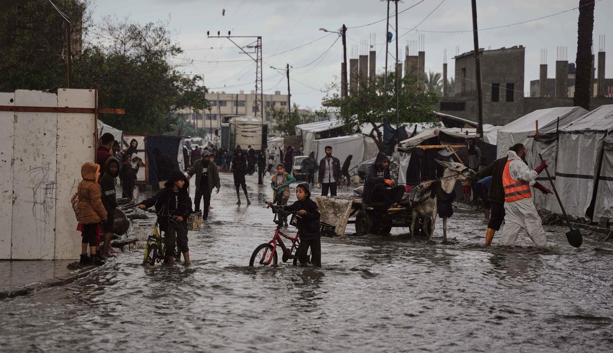 Warga Palestina berjalan di jalanan yang terendam banjir di samping kamp tenda sementara setelah hujan deras di Deir al-Balah, Jalur Gaza tengah, Selasa 25 November 2025. Banjir kembali menggenangi sebagian wilayah Deir al-Balah, Jalur Gaza tengah, pada Selasa 25 November 2025. (AP Photo/Abdel Kareem Hana)