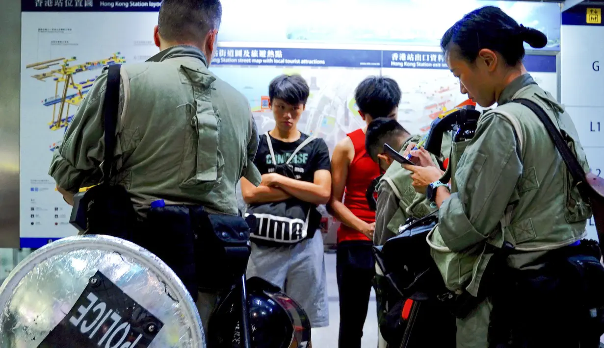 Polisi anti huru-hara memeriksa tas penumpang di stasiun pusat ekspres bandara di pusat kota Hong Kong, Sabtu (7/9/2019). Pengunjuk rasa pro-demokrasi berencana mengganggu jaringan transportasi ke bandara pada 7 September. (AP Photo/Vincent Yu)