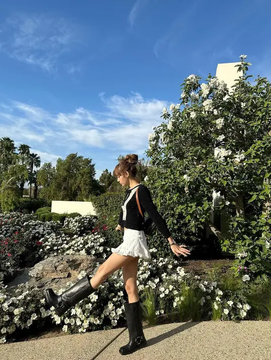 Lisa memadukan cropped blouse pita dan mini skirt putih, sepatu boots, serta tas ransel Celine. [Foto: IG/lalalalisa_m].