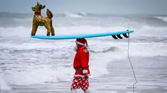 Seorang pengunjung berkostum Sinterklas bersiap untuk berselancar dalam acara Surfing Santa yang berlangsung di Pantai Cocoa, Florida, Amerika Serikat, Selasa (24/12/2024) waktu setempat. (AFP/Giorgio Viera)
