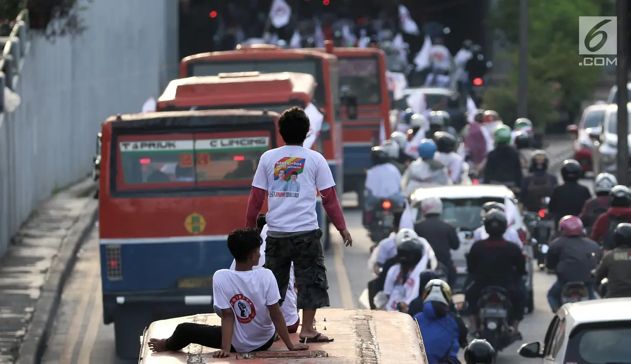 Relawan capres dan cawapres nomor urut 01 Joko Widodo atau Jokowi dan Ma'ruf Amin naik di atas bus saat konvoi menuju lokasi debat Pilpres 2019 di Jakarta, Minggu (17/2). Massa memberi dukungan untuk Jokowi yang akan berdebat. (Liputan6.com/JohanTallo)