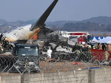 Petugas pemadam kebakaran dan petugas penyelamat bekerja di dekat reruntuhan pesawat Jeju Air Boeing 737-800 di Bandara Internasional Muan di Provinsi Jeolla Selatan, sekitar 288 kilometer sebelah barat daya Seoul pada tanggal 29 Desember 2024. (JUNG YEON-JE/AFP)